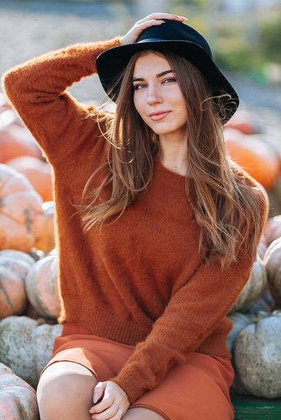 Portrait of happy woman sitting on farmers market with orange pumpkin in brown sweater and hat. Cozy autumn vibes Halloween, Thanksgiving day - Foto, imagen