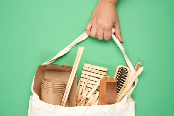 female hand holds full textile bag of recyclable household items, green background, zero waste  - Valokuva, kuva