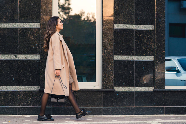 Fashionable žena s dlouhými vlasy procházky ve městě. Žena nosí módní kabát a boty. Pouliční. Mladá obchodnice kráčí po ulici. Ženská móda. - Fotografie, Obrázek