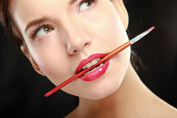 Woman's lips holding make up brush - Foto, afbeelding