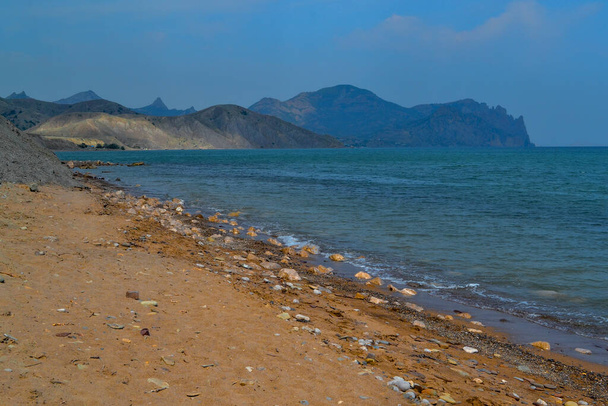 view of beautiful red sand pebbles coast of bay of Black sea with blue emerald water among hills and high mountains. Crimea, summer landscape - Valokuva, kuva