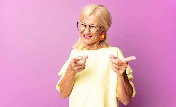 donna di mezza età sorridente con un atteggiamento positivo, di successo, felice che punta alla fotocamera, facendo segno di pistola con le mani - Foto, immagini