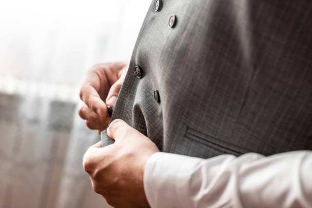 groom fastens a button on his vest at the groom's morning gatherings.the groom fastens the button. wedding day. gray jacket. hands of the groom, Grooms morning preparation. - Foto, Imagen