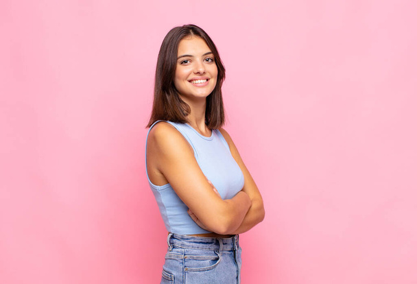 young pretty woman smiling to camera with crossed arms and a happy, confident, satisfied expression, lateral view - Фото, зображення