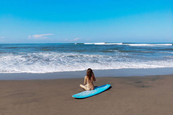 beautiful sporty surfing woman in sexy bikini sit near longboard surf surfboard board on beach before surfing. Modern active sport lifestyle and summer vacation. - Photo, Image