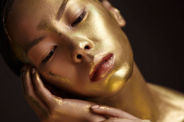 Beauty portrait of a beautiful asian girl with gold paint on her face against a dark background. - Zdjęcie, obraz