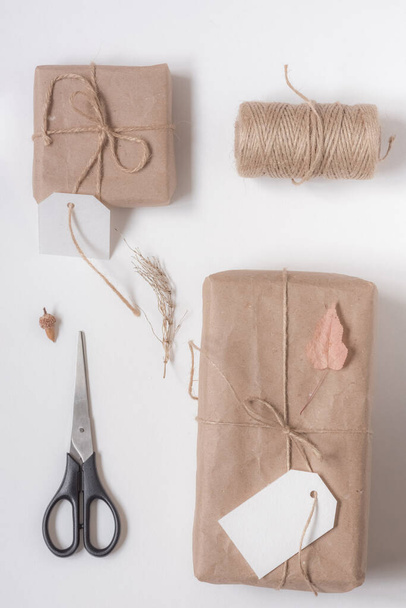Autumn holidays gifts composition. Gifts packed with eco-friendly natural materials, a spool of twine, scissors on a white background. Flat lay, top view - Fotó, kép