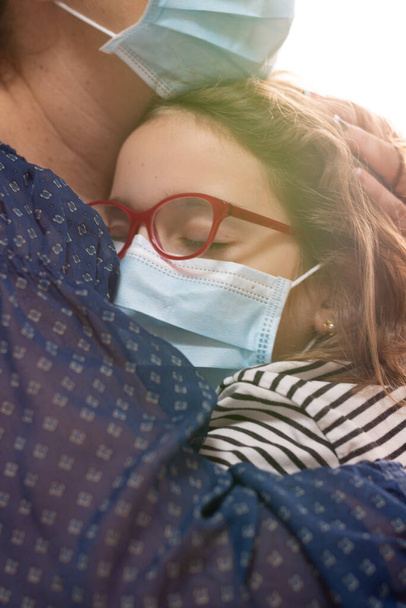 Frau tröstet an Coronavirus erkranktes Mädchen mit Maske, umarmt ihr Haar - Foto, Bild