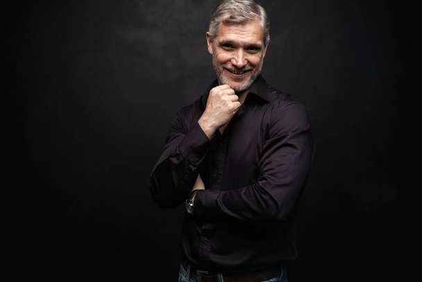Middle-aged good looking man posing in front of a black background with copy space. - Photo, image