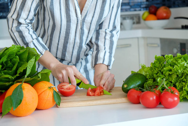 Cropped shot of unrecognizable woman cutting various fruits, vegetables, herbs and greens at her kitchen. Professional cook slicing ingredients. Vegan food concept. Close up, copy space, background. - Фото, зображення