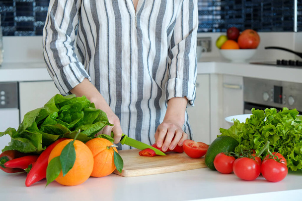Cropped shot of unrecognizable woman cutting various fruits, vegetables, herbs and greens at her kitchen. Professional cook slicing ingredients. Vegan food concept. Close up, copy space, background. - Foto, Imagen