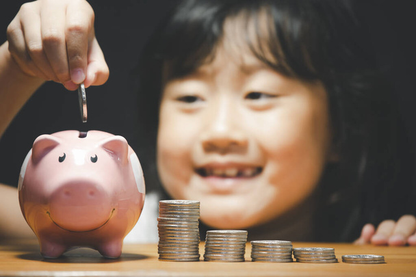 Aziatisch meisje met een munt te zetten in een spaarvarken bank in close-up en munten stapel, Besparen ideeën en investeringsbudget, Zakelijk spaargeld concept, Kopieer ruimte - Foto, afbeelding