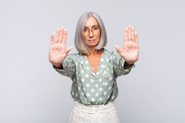 gray haired woman looking serious, unhappy, angry and displeased forbidding entry or saying stop with both open palms - 写真・画像