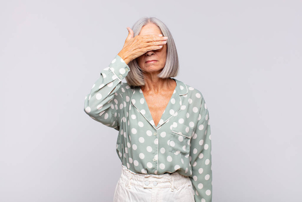 gray haired woman covering eyes with one hand feeling scared or anxious, wondering or blindly waiting for a surprise - Photo, Image