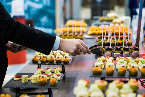 a man takes a canape with tongs from a tray during a coffee break - Photo, Image