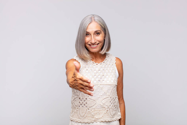 gray haired woman smiling, looking happy, confident and friendly, offering a handshake to close a deal, cooperating - Foto, Imagen