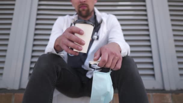 Руки крупним планом з чашкою кави та захисною медичною маскою розслабляються після одужання пацієнтів та важкої роботи. Медичний працівник відчуває себе втомленим після захисту та боротьби з ковадлом 19 з гарячим, енергійним напоєм
 - Кадри, відео