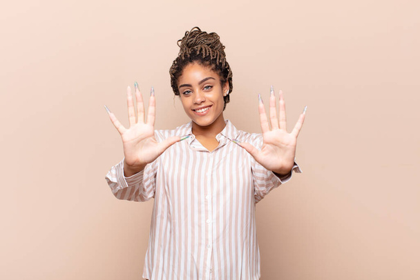 young afro woman smiling and looking friendly, showing number ten or tenth with hand forward, counting down - Photo, Image