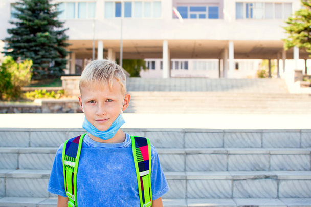 Щасливий усміхнений школяр на фоні школи. Шкільний хлопчик носить медичну маску для захисту обличчя. Повернутися до школи. Концепція навчання
 - Фото, зображення