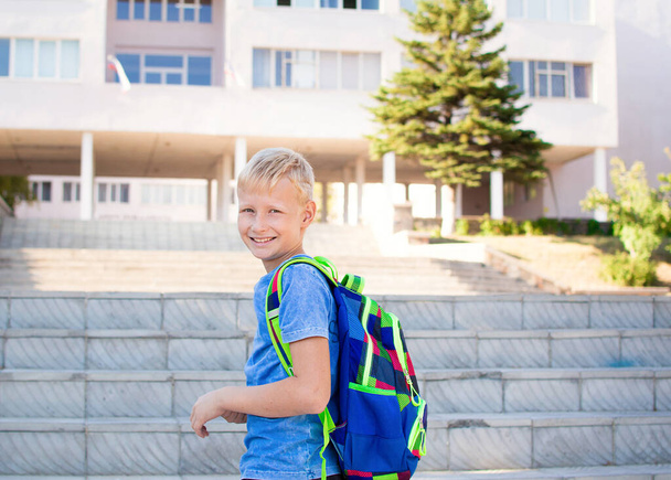 Счастливый улыбающийся школьник с рюкзаком на фоне школы. Возвращайся в школу. Концепция обучения - Фото, изображение