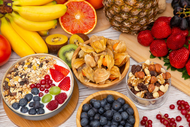Ryhmä Hedelmät Aamiainen sekoitetut vihannekset salaattikulholla, pähkinäkulholla, mansikalla, banaanilla ja ananaksella, appelsiinimehu, c-vitamiini elintarvikkeissa luonto terveydelle ja ruokavaliolle ylhäältä näkymä puupöydälle. - Valokuva, kuva