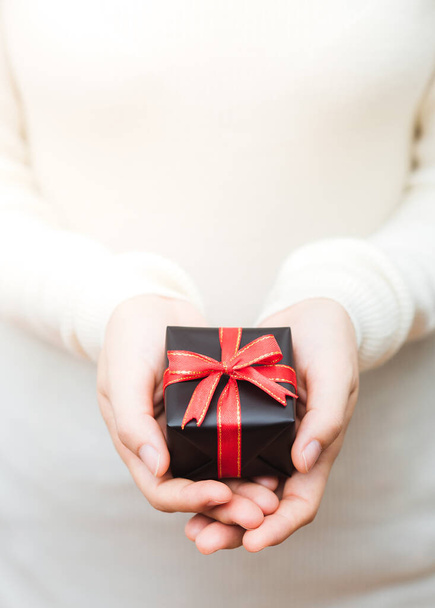 Close up shot of female hands holding a small gift wrapped with red ribbon.  - Photo, image