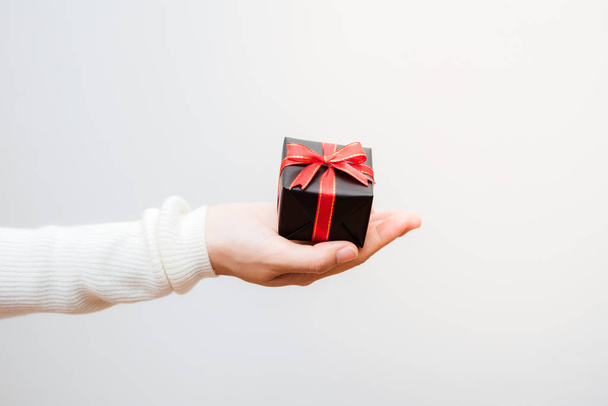 Primer plano de las manos femeninas sosteniendo un pequeño regalo envuelto con cinta roja.  - Foto, Imagen