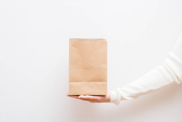 Packaging template mock up. Delivery service concept. Copy space. Advertising area banner. Close up female holds in hand brown clear empty blank craft eco paper bag on white background. - Photo, Image