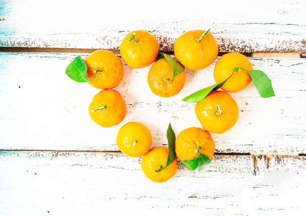 Small tangerines are laid out in the shape of a heart and lie on a white wooden table. Healthy food concept. - Foto, Imagen