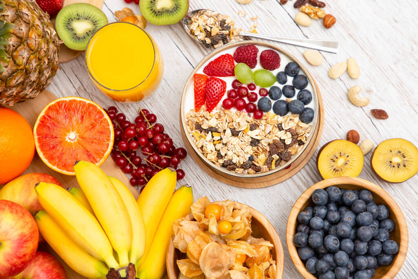 Ryhmä Hedelmät Aamiainen sekoitetut vihannekset salaattikulholla, pähkinäkulholla, mansikalla, banaanilla ja ananaksella, appelsiinimehu, c-vitamiini elintarvikkeissa luonto terveydelle ja ruokavaliolle ylhäältä näkymä puupöydälle. - Valokuva, kuva