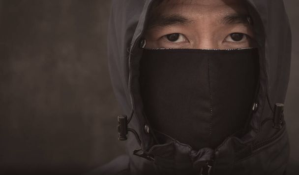 Το πρόσωπο του Ασιάτη φορώντας μάσκα ύφασμα για την πρόληψη PM 2.5 σκόνη και μικρόβια νέφος, τοξικές αναθυμιάσεις, και τη σκόνη, την πρόληψη της βακτηριακής λοίμωξης του ιού Corona ή Covid 19 στο μαύρο φόντο. - Φωτογραφία, εικόνα