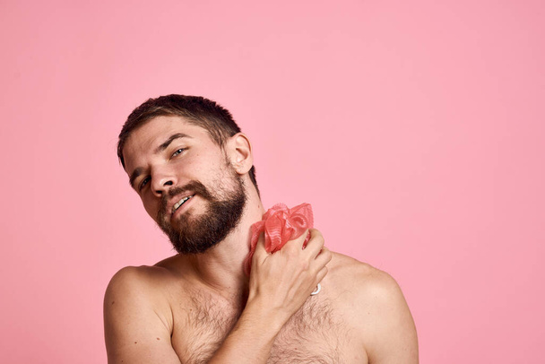 手に洗濯布で裸の肩を持つ男シャワークリーンな肌ピンクの背景 - 写真・画像