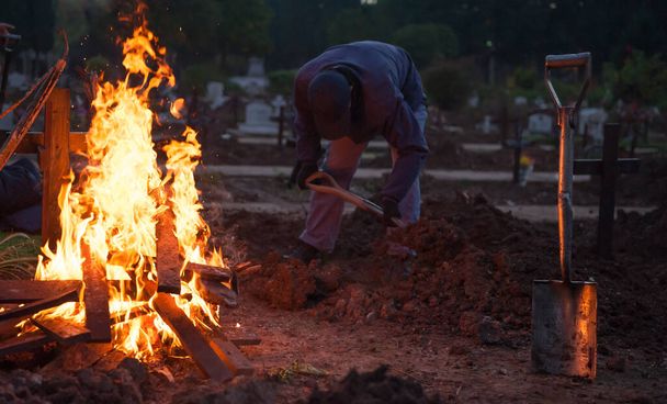 Operai del cimitero che scavano per estrarre i resti umani e croci in fiamme - Foto, immagini