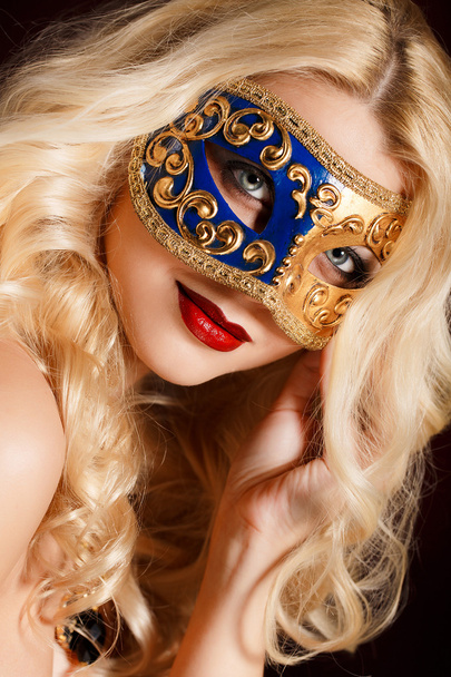 Portret van een mooie jonge blonde vrouw met theatrale masker op zijn gezicht op een donkere achtergrond - Foto, afbeelding