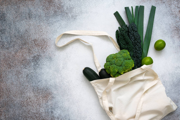 Green vegetables in eco shopping bag on concrete background. Zucchini, broccoli, kale, limes and leek. Zero waste. Healthy lifestyle concept. - Zdjęcie, obraz