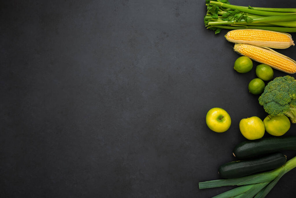 Top view of celery, corn, broccoli, apples, zucchinis, leek and limes. Various vegetables on black background with copy space. Healthy lifestyle. - Photo, image
