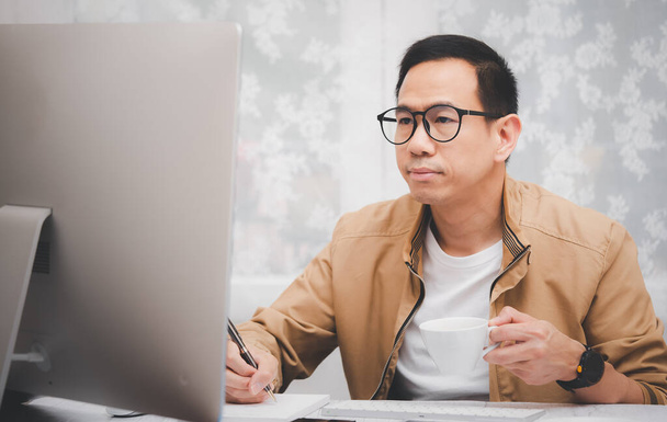 Hombre asiático en ropa casual utilizando un ordenador portátil se comunica en Internet con el cliente en la mesa de la cocina en casa. trabajo conceptual desde casa. - Foto, Imagen