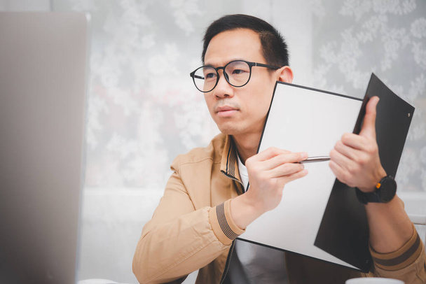 Homem asiático em roupas casuais usando um laptop se comunica na internet com o cliente na mesa da cozinha em casa. trabalho conceito a partir de casa. - Foto, Imagem