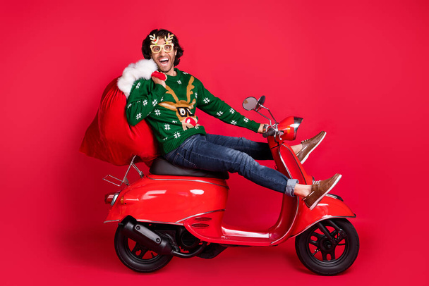 Profile side view of attractive childish comic cheerful carefree guy riding moped delivering gifts sack December tradition having fun fooling isolated bright vivid shine vibrant red color background - Фото, изображение