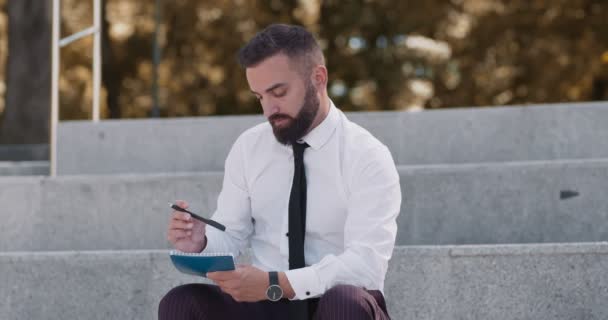 Hombre de negocios de mediana edad escribiendo notas, pensando en el plan financiero en el parque - Imágenes, Vídeo
