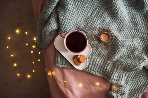 Egy csésze friss kávé finom sütikkel gyertyával és világító lámpákkal kötött pulóveren az ágyban, közelről. - Jó reggelt! Reggeli idő. Őszi szezon. Felülnézet.  - Fotó, kép