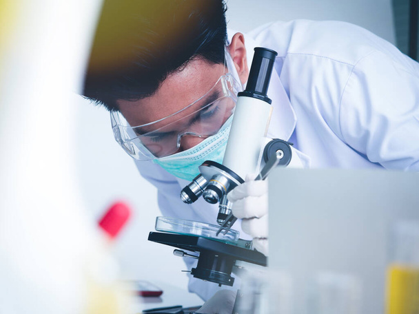 Aziatische mannelijke wetenschapper werkt serieus Chemie experiment Met een microscoop In het laboratorium, de kleur toon beeld. - Foto, afbeelding