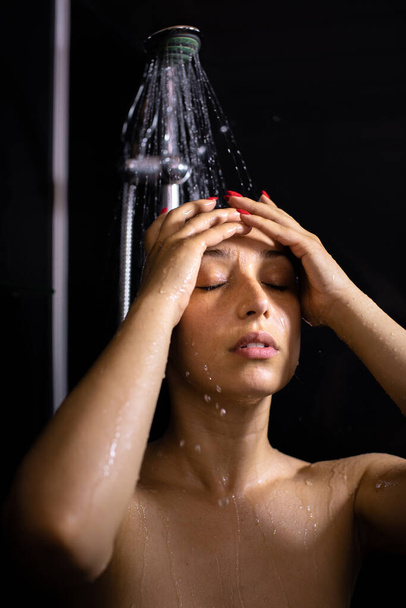 Όμορφη νεαρή γυναίκα απολαμβάνει τη ροή του νερού, κάνοντας ντους, κλείνοντας τα μάτια - Φωτογραφία, εικόνα