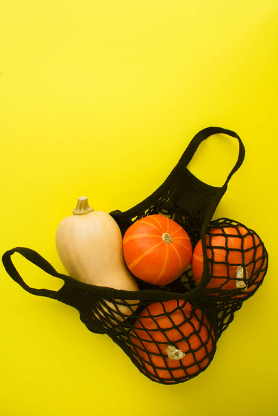 No plastic bag concept. Mesh shopping black bag with pumpkin  on the yellow background. Copy space. Location vertical. - Fotoğraf, Görsel
