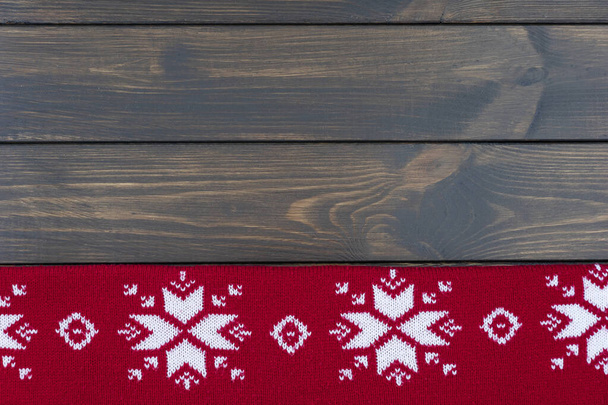 πλεκτή κόκκινη κουβέρτα με παραδοσιακό χριστουγεννιάτικο σχέδιο στο κάτω μέρος σε σκούρο ξύλινο φόντο. Αντιγραφή χώρου για κείμενο. - Φωτογραφία, εικόνα