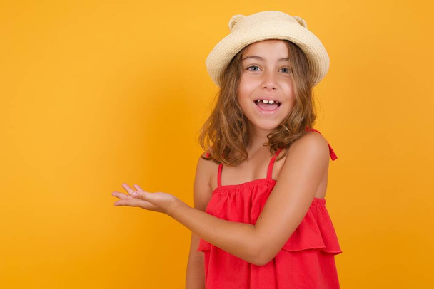 cute little girl wearing red dress showing something  on yellow background  - Foto, Bild