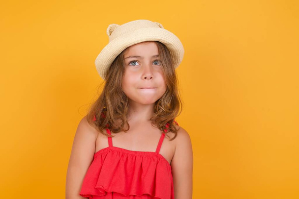 cute little girl wearing red dress thinking  on yellow background  - Φωτογραφία, εικόνα