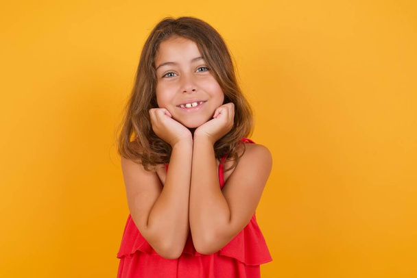 söpö pieni tyttö yllään punainen mekko hymyilee keltaisella taustalla  - Valokuva, kuva