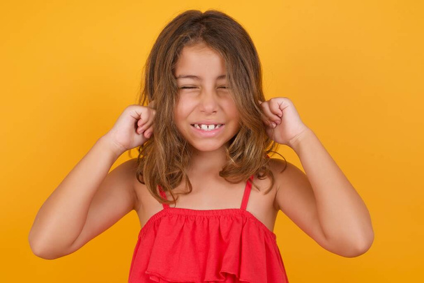 cute little girl wearing red dress closing ears  on yellow background  - Foto, Imagen
