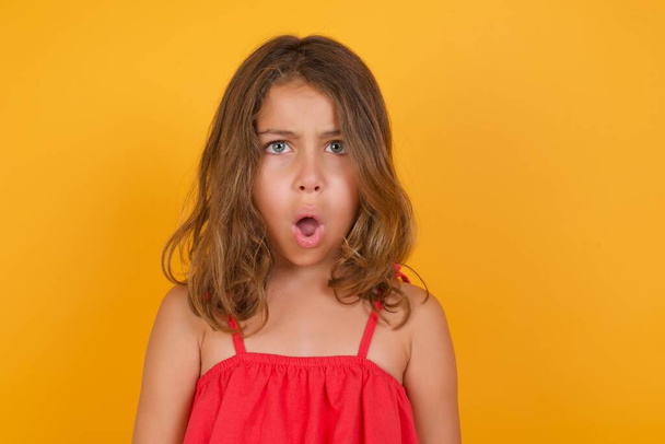 cute little girl wearing red dress with open mouth on yellow background  - Foto, afbeelding